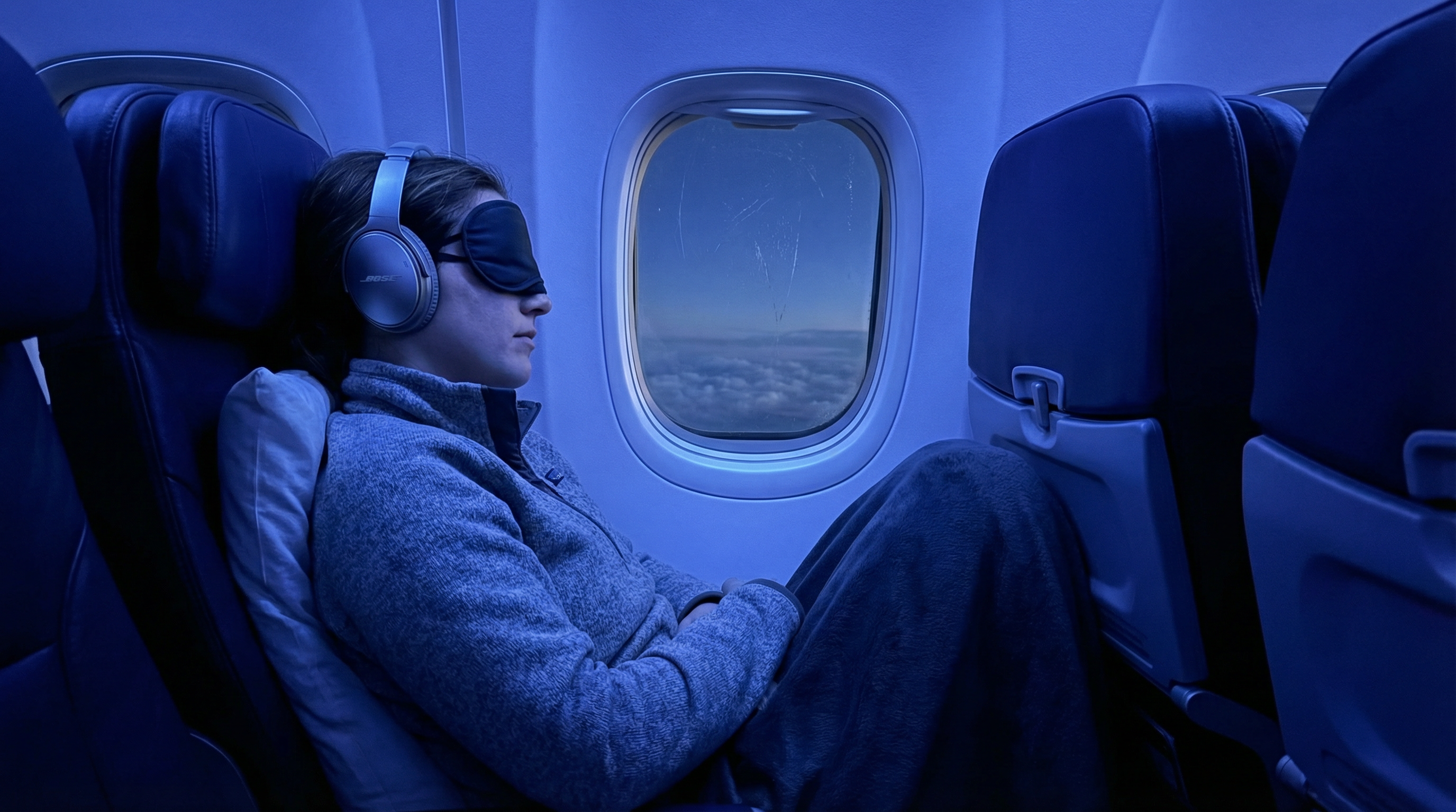 Dica: Um passageiro relaxado a dormir no seu lugar à janela do avião, a usar uns grandes auscultadores de cancelamento de ruído e uma camisola confortável
