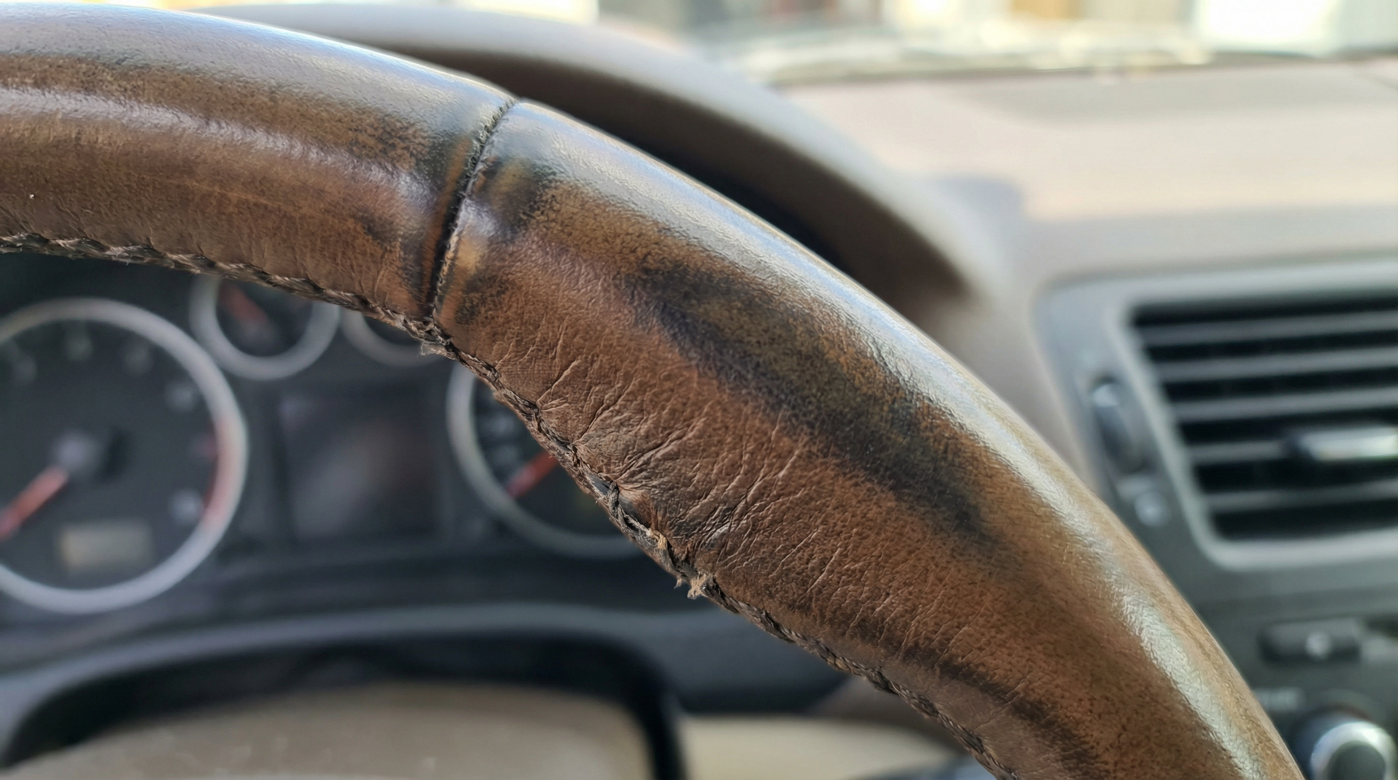 Dica: Um close-up detalhado de um volante em pele visivelmente gasto, polido e liso pelo uso intenso de milhares de quilómetros.